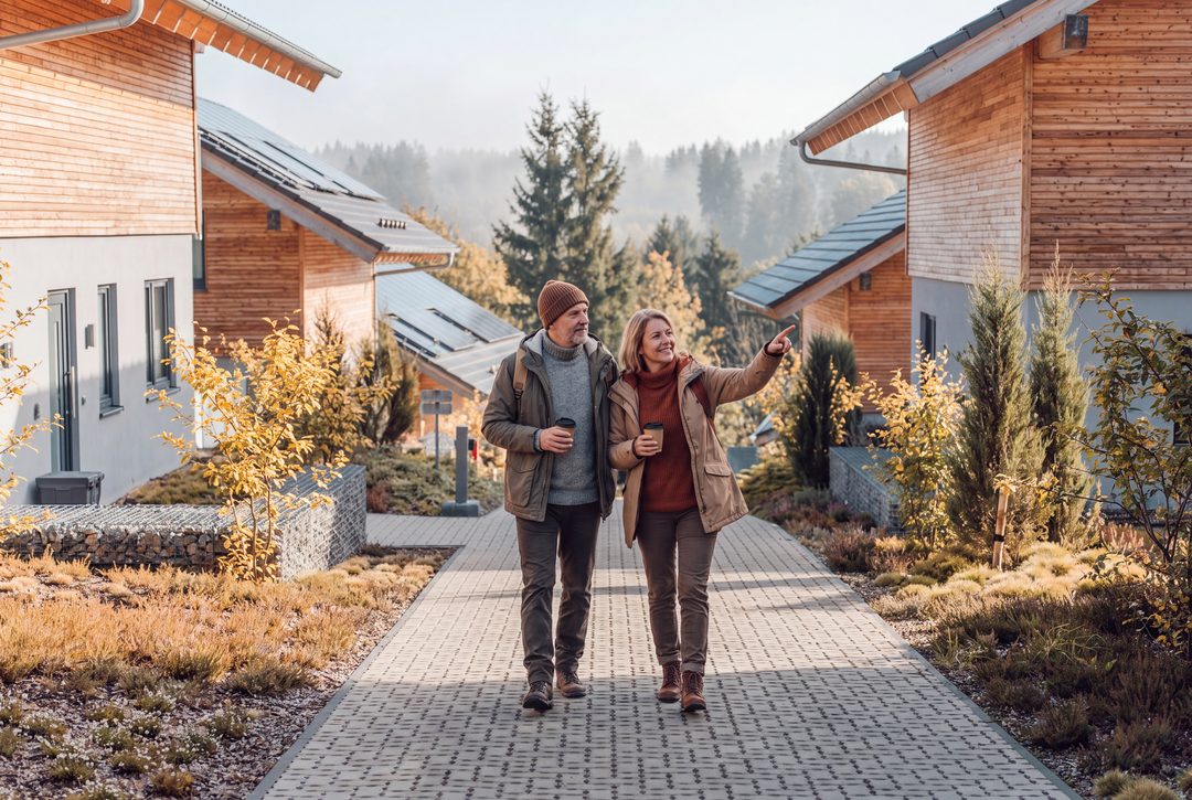 Una pareja con tazas de café da un paseo una mañana de otoño por el camino que hay entre los chalets; la mujer señala las colinas boscosas, imagen ilustrativa