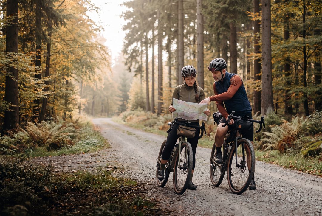 Generierte, Harz-inspirierte Szene: zwei Gravelbiker planen an einer Waldkreuzung mit einer Wanderkarte die nächste Etappe, Symbolbild