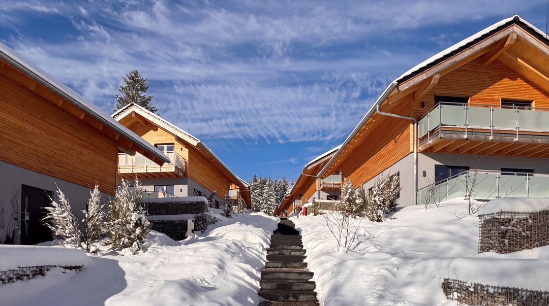 Escalera nevada entre chalets revestidos de madera en invierno, bajo el sol