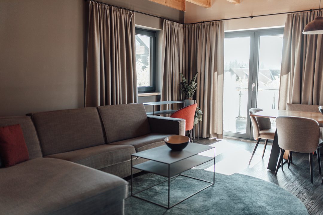 Salón diáfano de un chalet con sofá gris, mesa de centro, mesa de comedor y puerta que da a la terraza, con luz natural