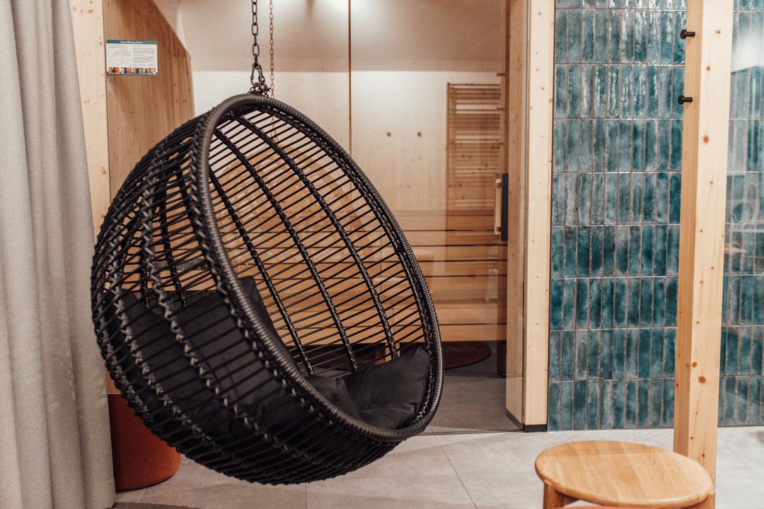 Silla colgante y taburete delante de la puerta de cristal de la sauna de uno de los chalets