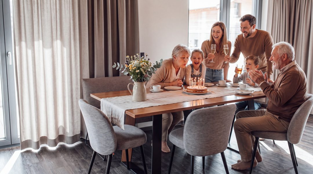 Familienfeier im Chalet: Die Großmutter bläst am langen Esstisch die Kerzen auf ihrem Geburtstagskuchen aus, Enkel, Eltern und Großvater feiern mit, Symbolbild
