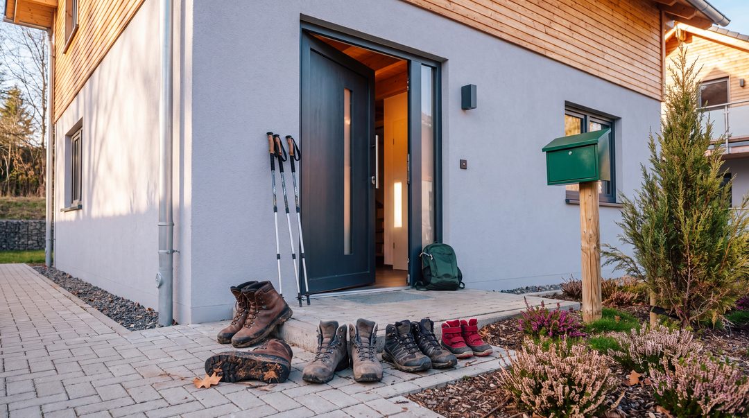 Después de la ruta de senderismo, hay varios pares de botas de montaña delante de la puerta abierta de un chalet, con los bastones de senderismo apoyados al lado; imagen ilustrativa