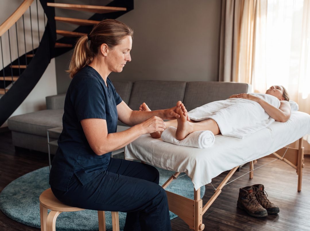 Fodmassage efter en vandretur: Terapeuten sidder ved fodenden af briksen, ved siden af står vandrestøvler, symbolbillede