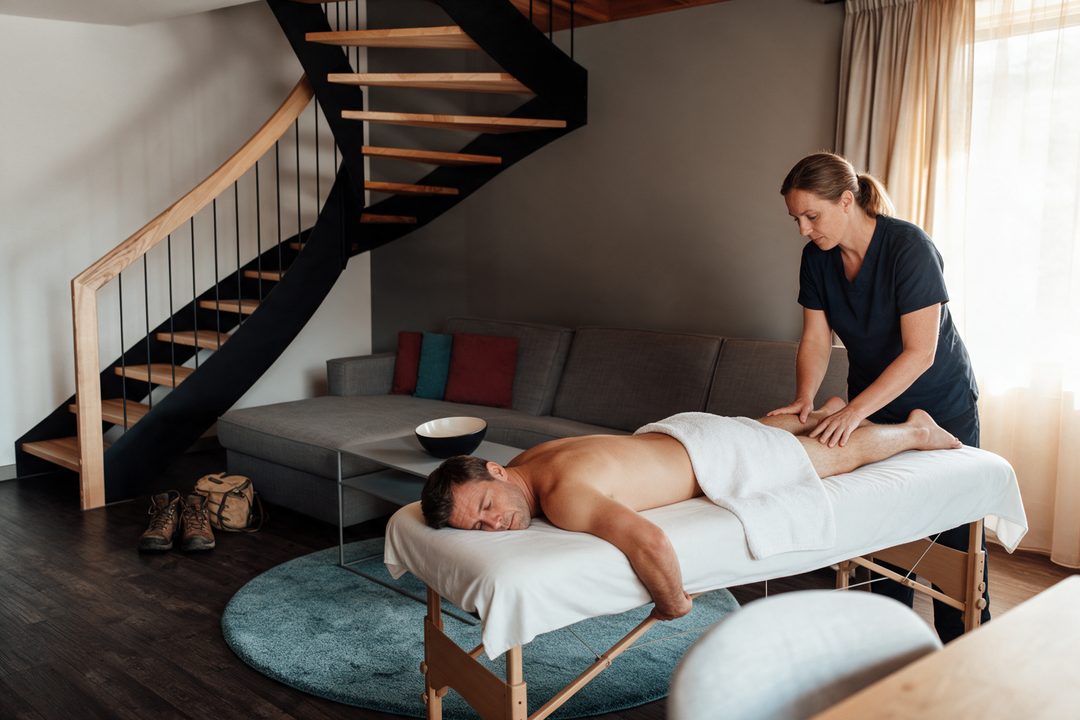 Benmassage efter en vandretur i stuen i et chalet, vandrestøvler ved trappen, symbolbillede