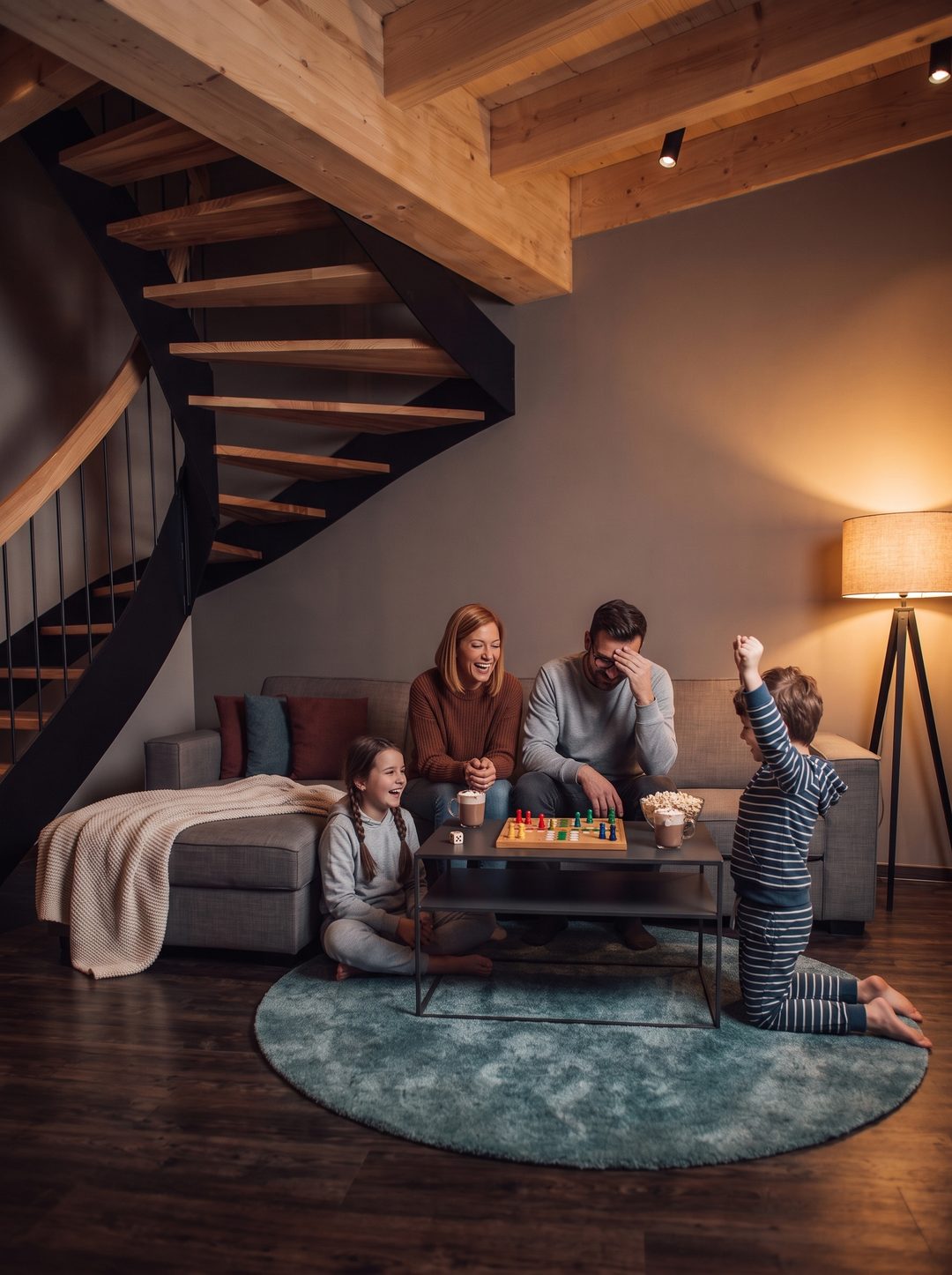 En familie spiller et brætspil om aftenen i stuen i et chalet under trappen, stående format, symbolbillede