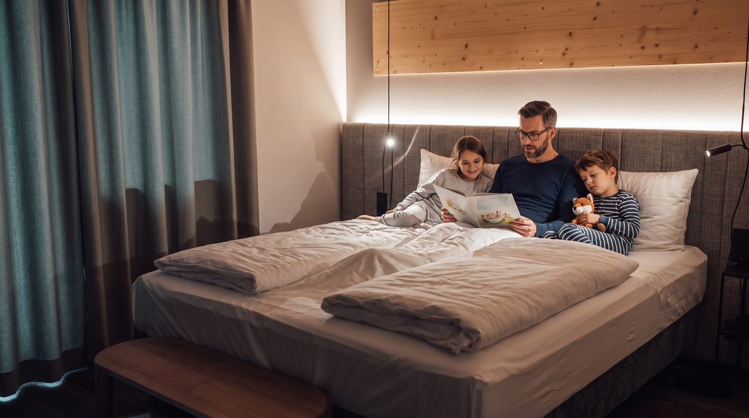 Far læser en godnathistorie højt for to børn i dobbeltsengen i et af chaletets soveværelser, symbolbillede