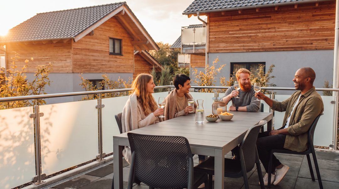 Fire venner med drikkevarer og tæpper på terrassen ved et chalet i aftenlyset, symbolbillede