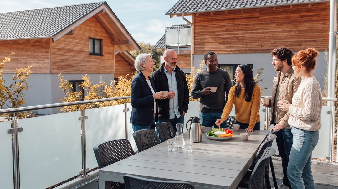 Teamet holder en munter kaffepause på terrassen ved et chalet; på bordet står der grøntsagssticks med dip og kaffe – symbolbillede