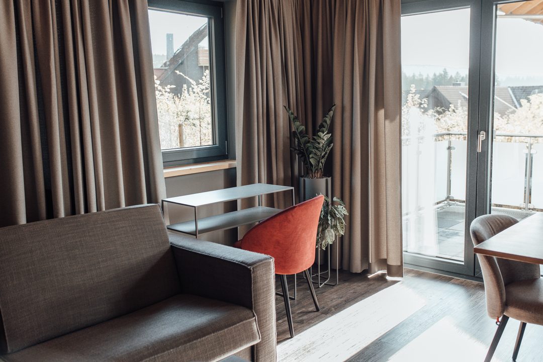 Rincón de sofás con un sillón naranja frente a la puerta de la terraza, con vistas al exterior