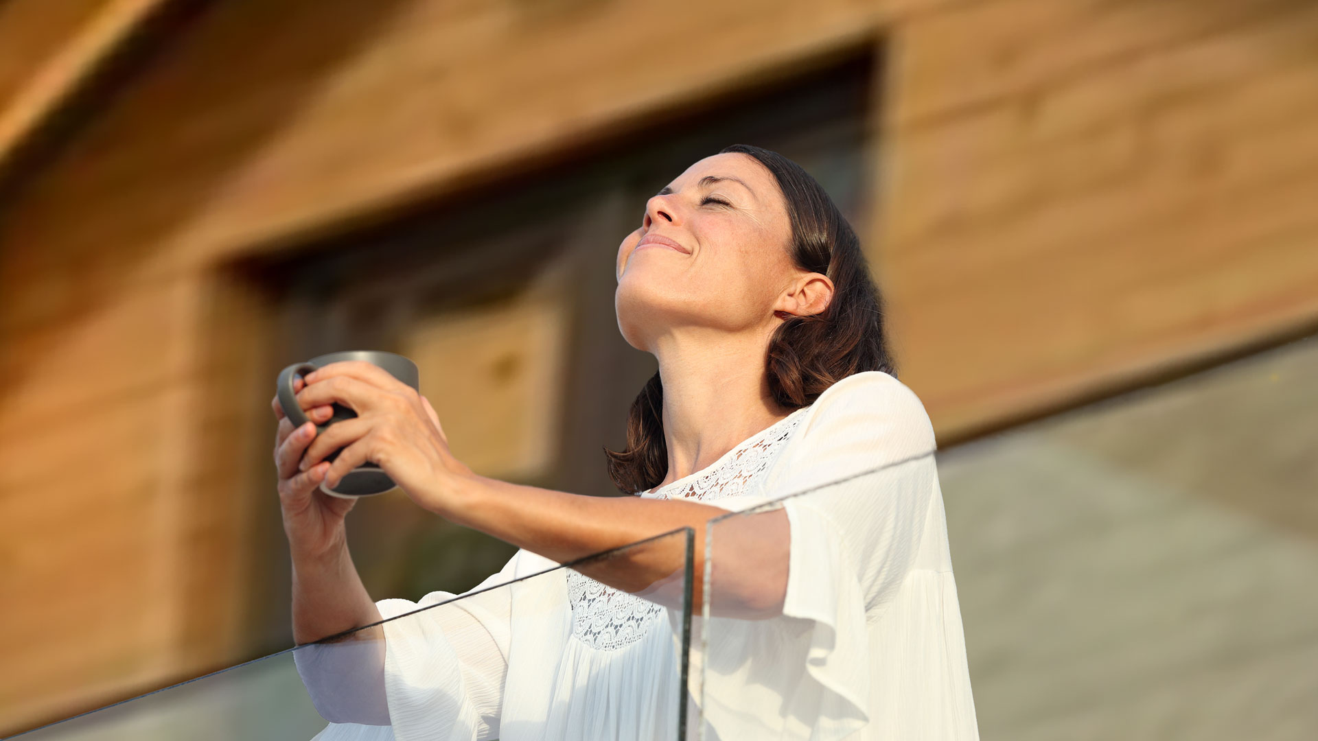 Eine Frau steht auf dem Balkon ihres Hanhneklee Ferienchalets und geniesst sichtlich einen Kaffee.